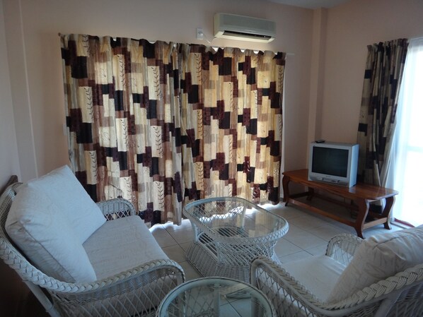 Un salón con muebles de mimbre, un televisor sobre un mueble de madera y una cortina estampada.