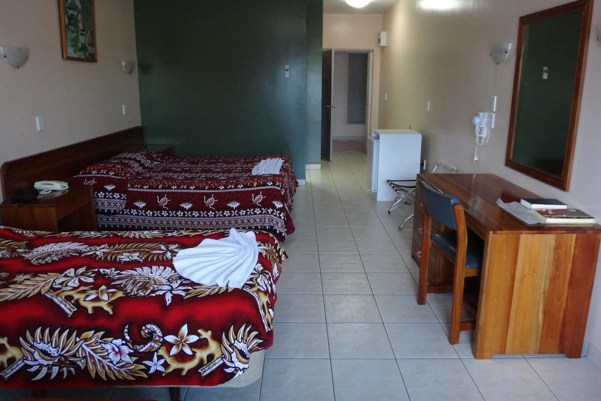 A hotel room with two beds, a desk, a chair, a mirror, and a small kitchenette.