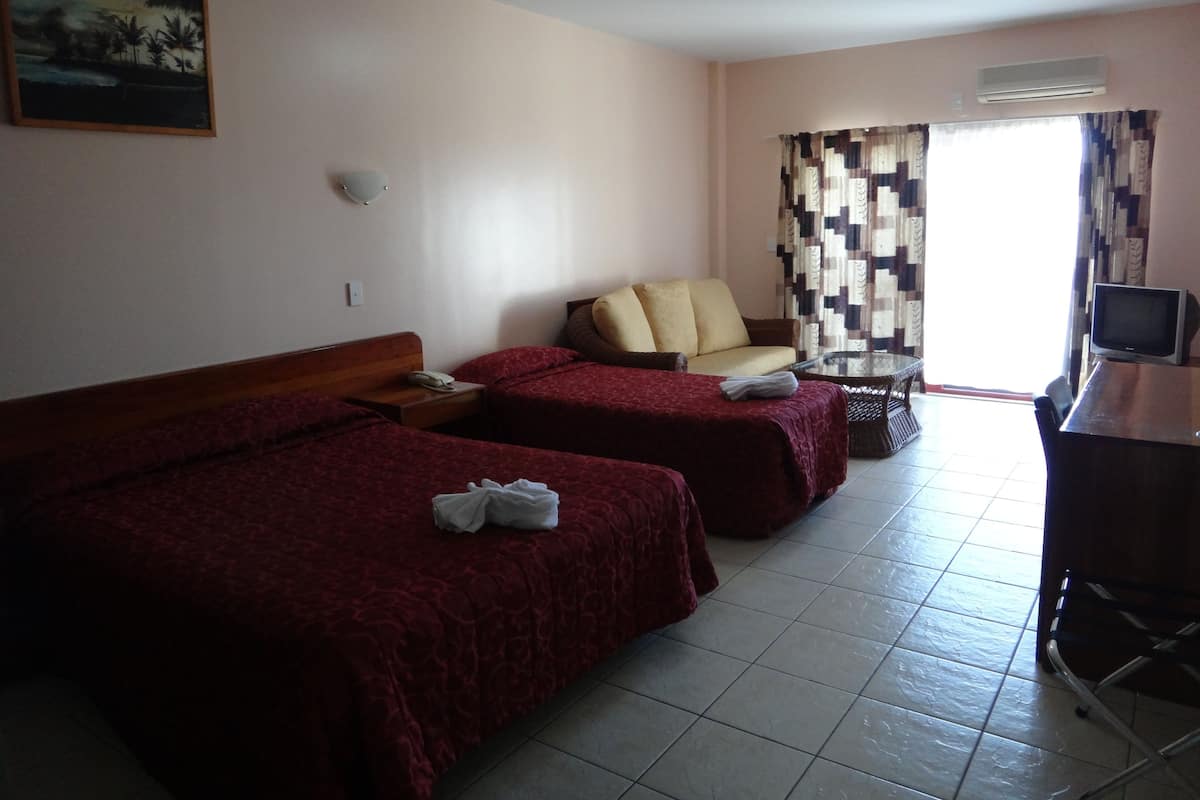 A hotel room with two single beds, a sofa, a TV, and a window with curtains.