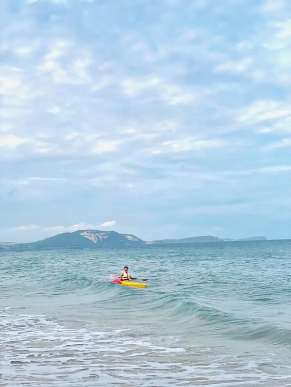 Un kayakista en un mar tranquilo con montañas lejanas y cielo despejado.