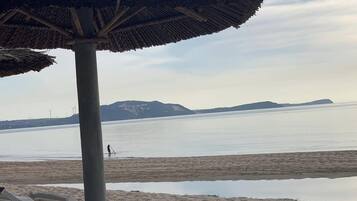 A beach with a thatched umbrella, lounge chairs, and a calm sea with distant mountains.