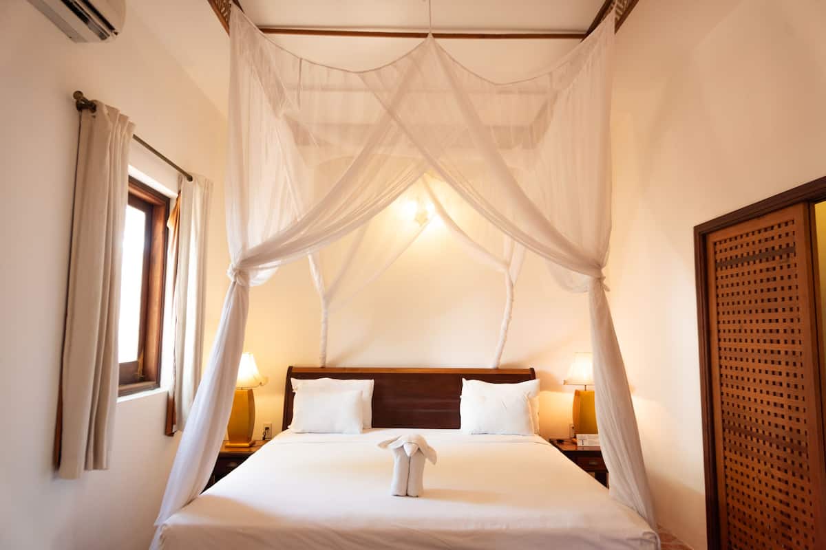 A hotel room with a four-poster bed, two bedside lamps, and a window with curtains.