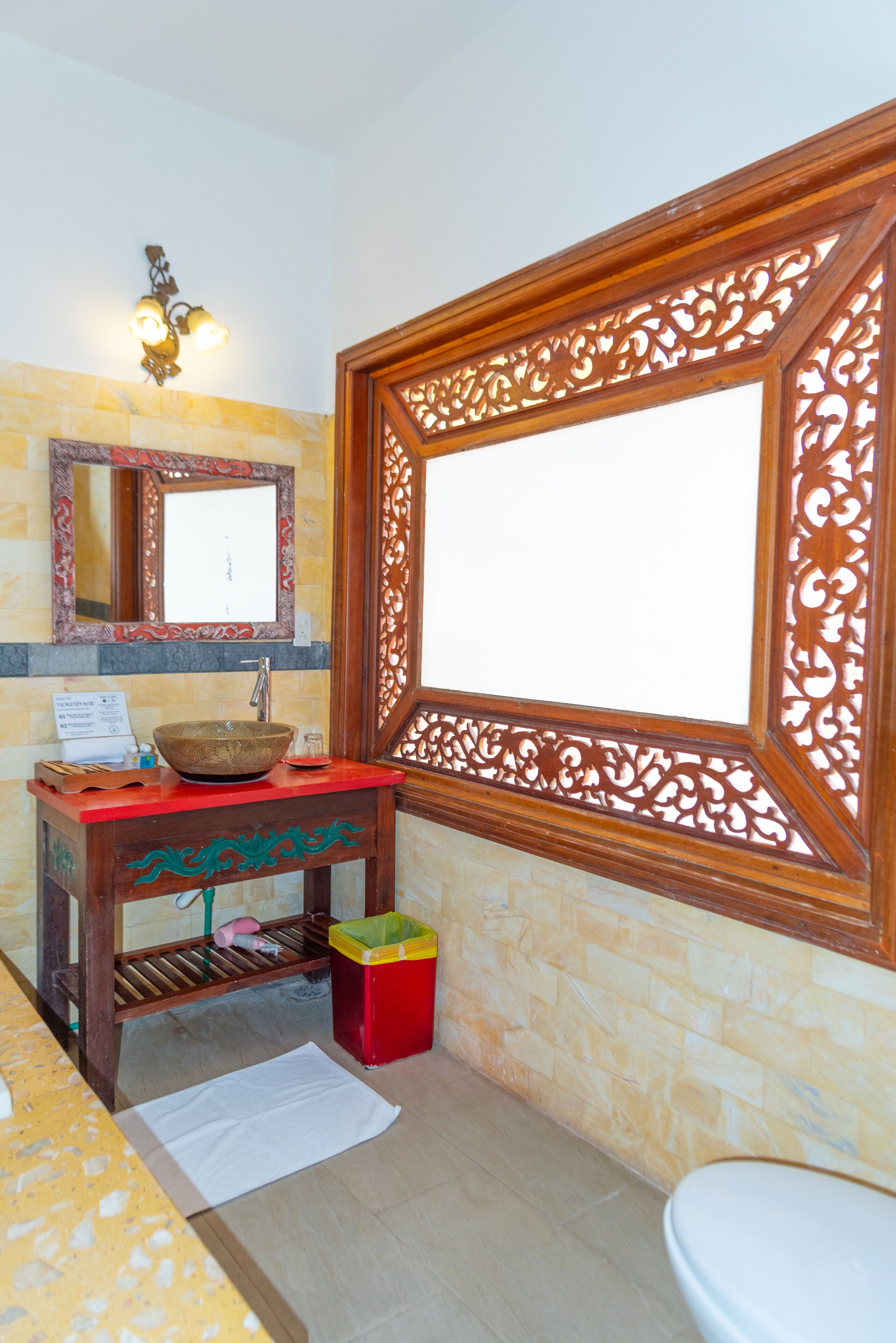A bathroom with a wooden vanity, a large mirror, a decorative wall panel, and a toilet.