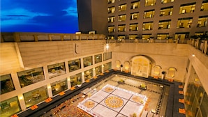 Un patio de hotel con una fuente central, zonas de estar alrededor y una gran entrada.