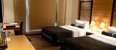 A hotel room with two beds, a desk, a telephone, and a window with blinds.