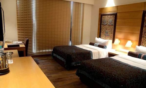 Une chambre d’hôtel avec deux lits, un bureau, un téléphone et une fenêtre avec des stores.