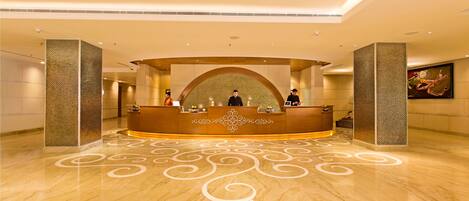 A hotel reception area with a curved desk, a patterned floor, and a large painting on the wall.