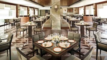 A spacious dining area with multiple tables set for service, a central marble column, and a high ceiling with wooden paneling.