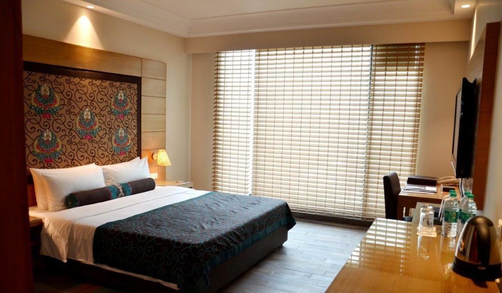 A hotel room with a bed, bedside table, lamp, and a desk with a chair.