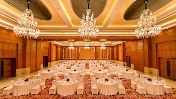 A large banquet hall with round tables, white chairs, and chandeliers.