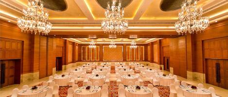 A large banquet hall with round tables, white chairs, and chandeliers.