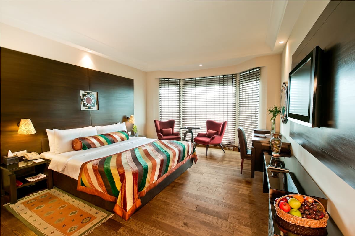 Ein Hotelzimmer mit einem großen Bett, einem Schreibtisch mit Stuhl, einem Fernseher und einem Fenster mit Jalousien.