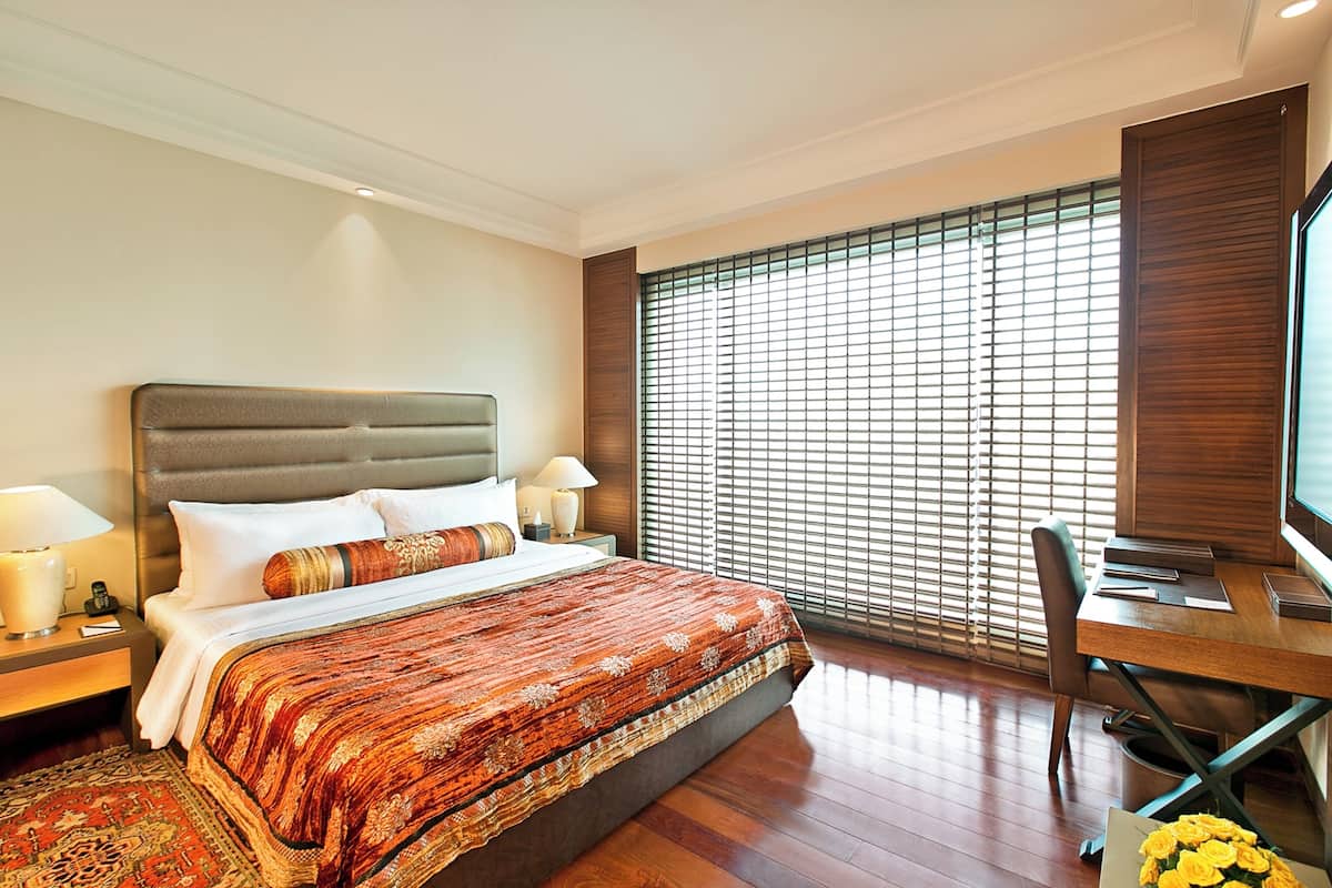 Ein Hotelzimmer mit einem großen Bett, einem Schreibtisch mit Stuhl, einem Fernseher und einem Fenster mit Jalousien.