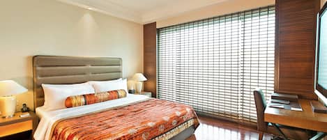 A hotel room with a large bed, a desk with a chair, a television, and a window with blinds.