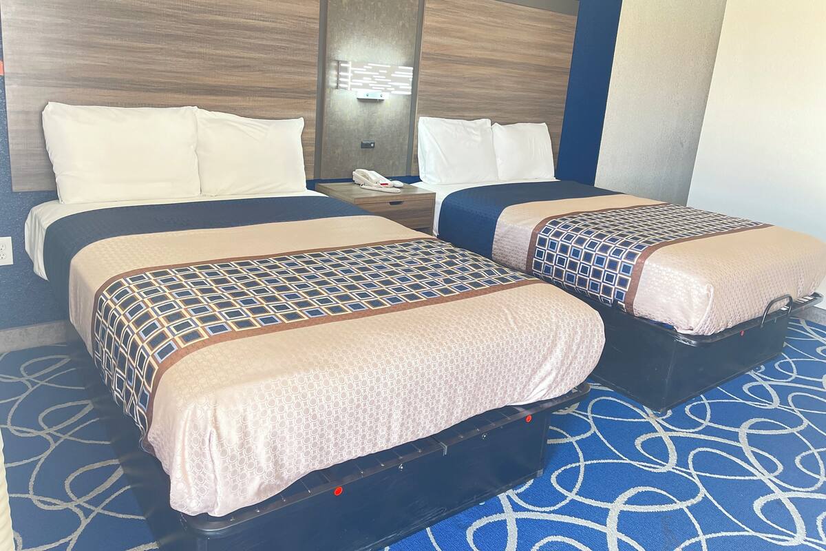 Una habitación de hotel con dos camas, una mesita de noche con teléfono y un espejo en la pared.
