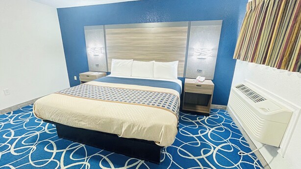 Une chambre d’hôtel comprenant un lit, deux tables de chevet, une tête de lit et un climatiseur fixé au mur.
