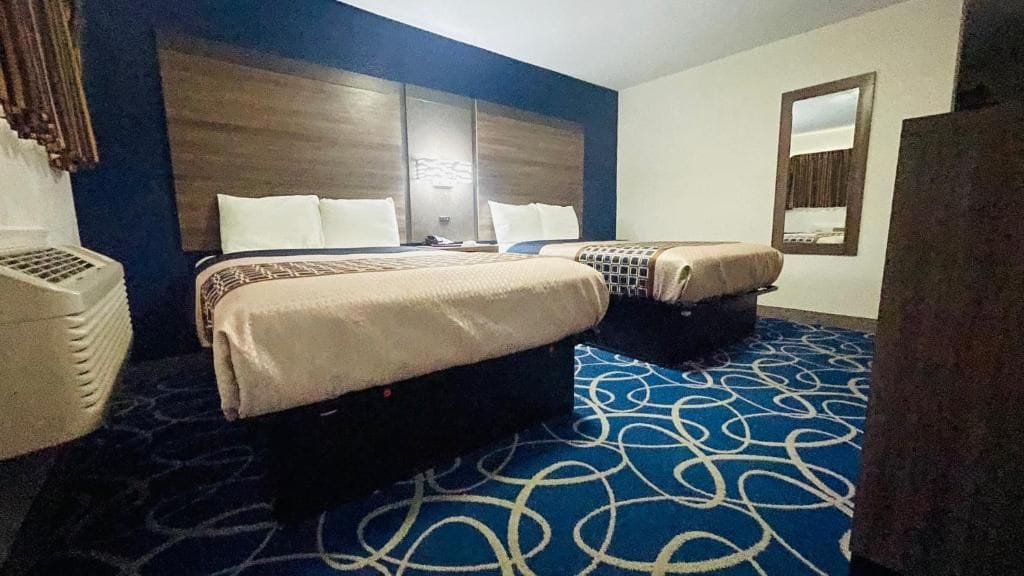 A hotel room with two beds, a large headboard, a patterned carpet, and a mirror on the wall.