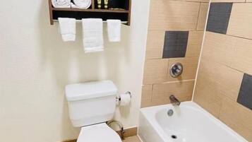 Un baño con inodoro, bañera y un estante con toallas.