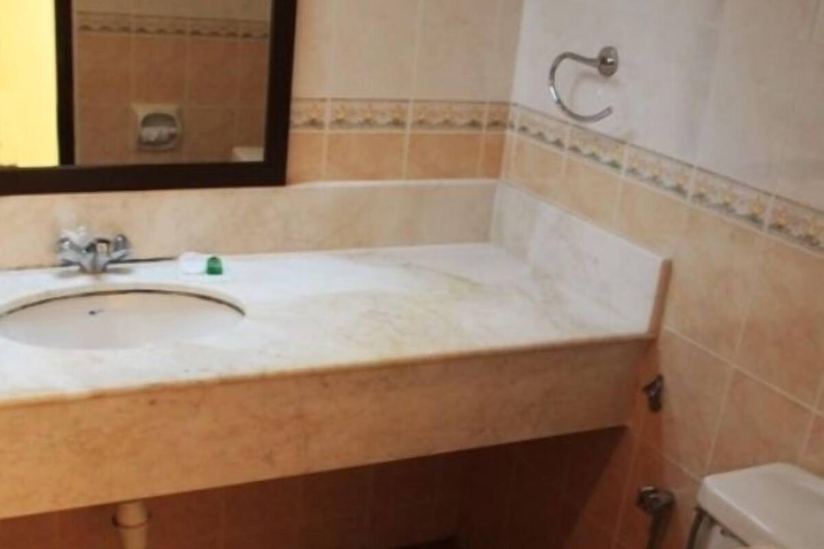 Casa de banho com lavatório, espelho, sanita e paredes revestidas a azulejos.