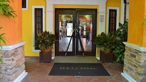 A hotel entrance with a yellow facade, a black doormat with "WELCOME" written on it, and potted plants on either side. - GeoPark Hotel (Langkawi)
