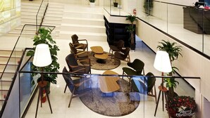 A modern lobby with a glass railing, seating area with chairs and a round table, and potted plants. - Urban Boutique Hotel (Anyang)