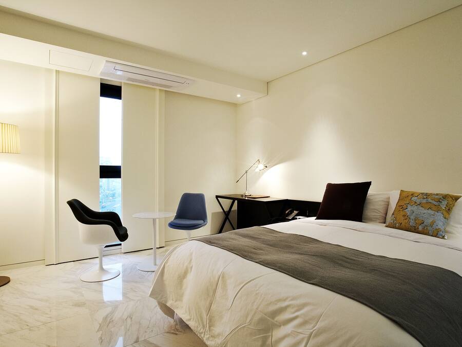 Una habitación de hotel moderna con una cama grande, un escritorio, una silla y una lámpara.