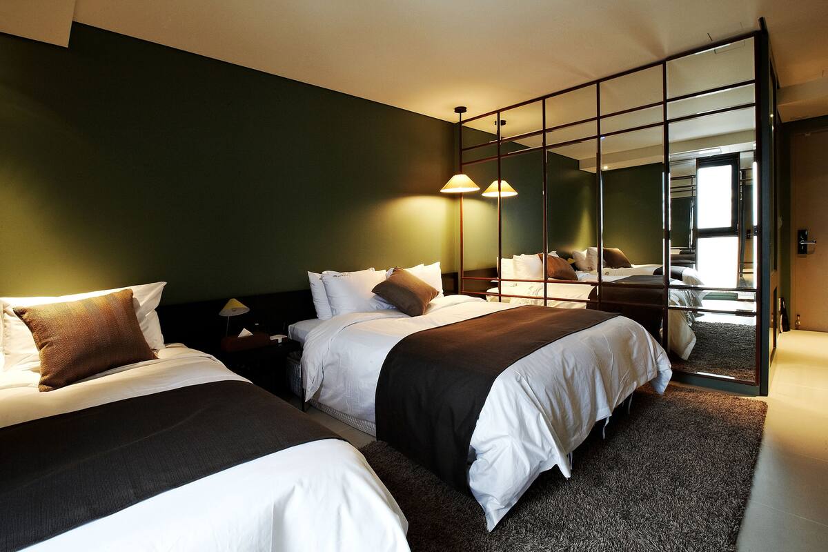 A hotel room with two beds, a large mirror, and a view of the city.