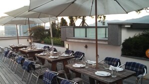 An outdoor dining area with wooden tables and chairs, umbrellas, and a view of the cityscape. - Urban Boutique Hotel (Anyang)