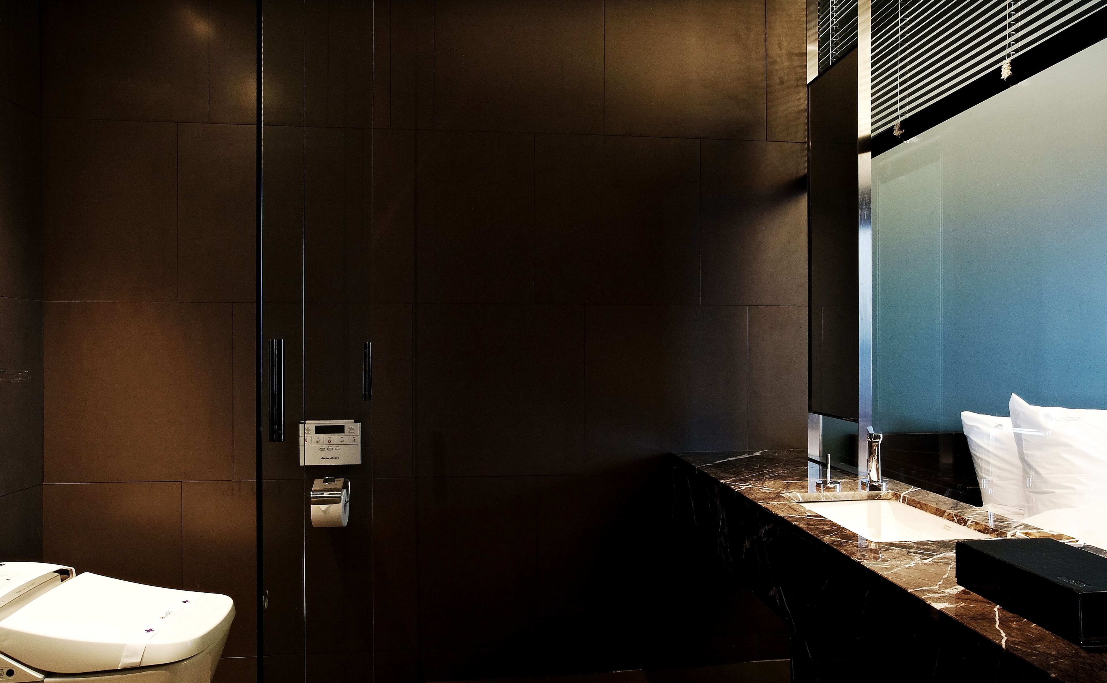 A modern bathroom with a dark tiled wall, a marble countertop, a sink, and a toilet.