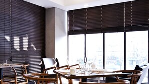 A modern dining area with a round table, wooden chairs, and large windows offering a city view. - Urban Boutique Hotel (Anyang)