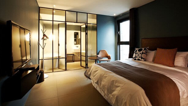 A modern hotel room with a large bed, a desk, and a glass partition separating the room from a bathroom. - Urban Boutique Hotel (Anyang)