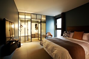 A modern hotel room with a large bed, a desk, and a glass partition separating the room from a bathroom. - Urban Boutique Hotel (Anyang)