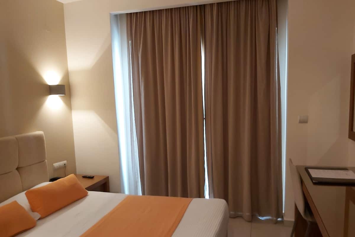 A hotel room with a bed, a desk, a lamp, and a window with curtains.
