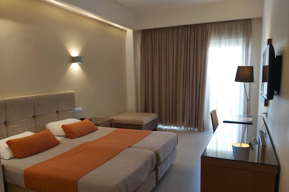 A hotel room with a large bed, a desk, a chair, a TV, and a window with curtains.