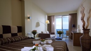 A hotel room with a large bed, a sitting area, and a view of the sea. - El Greco Hotel (Ierapetra)