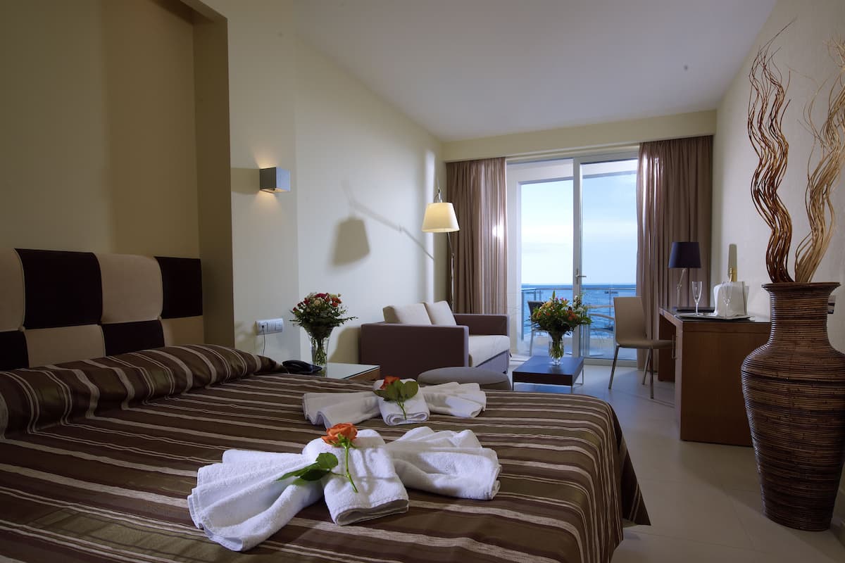 A hotel room with a large bed, a sitting area, and a view of the sea.
