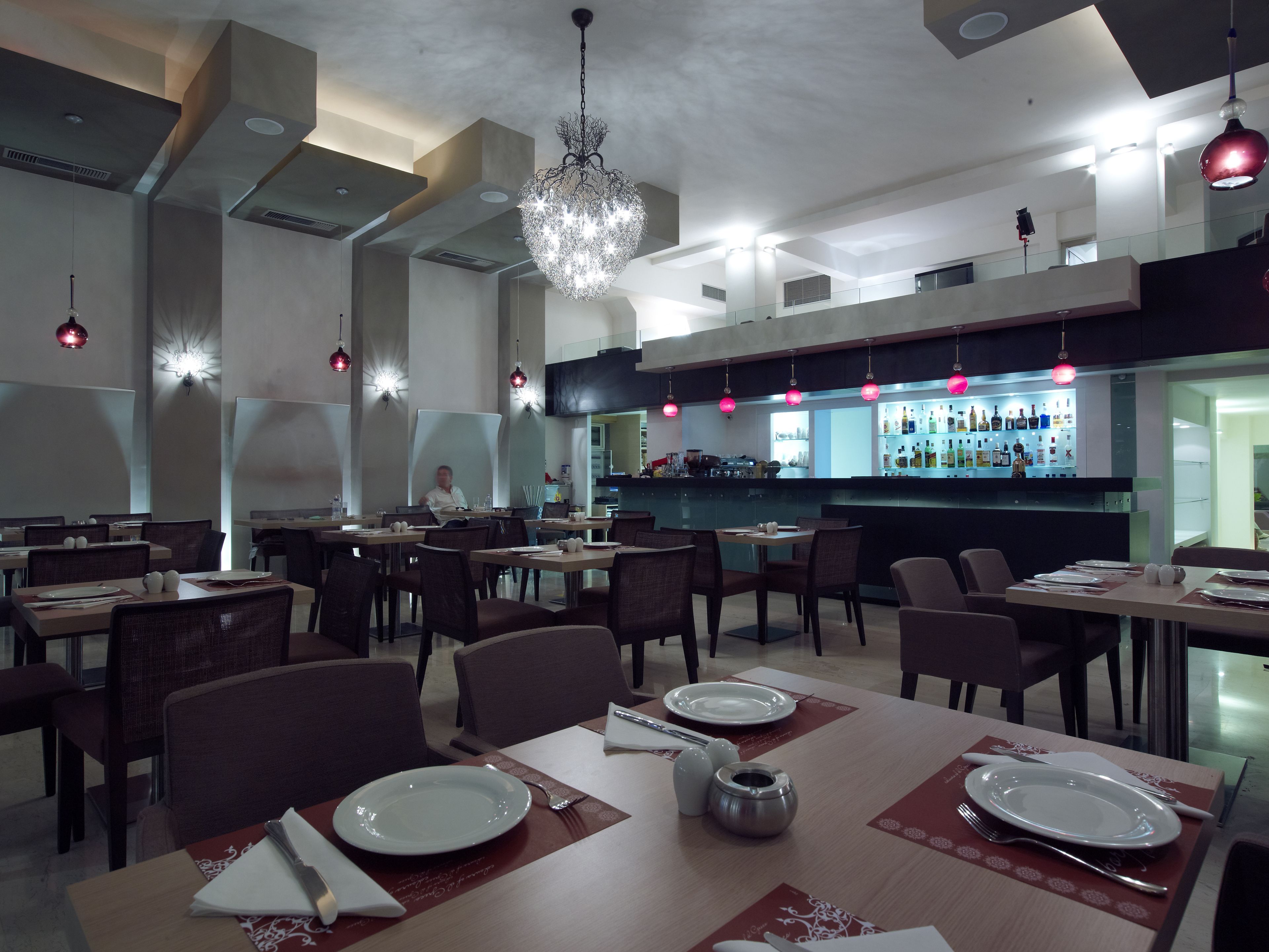A modern restaurant with high ceilings, pendant lighting, and a bar area.