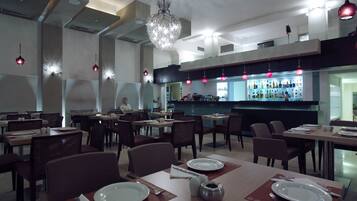A modern restaurant with high ceilings, pendant lighting, and a bar area.