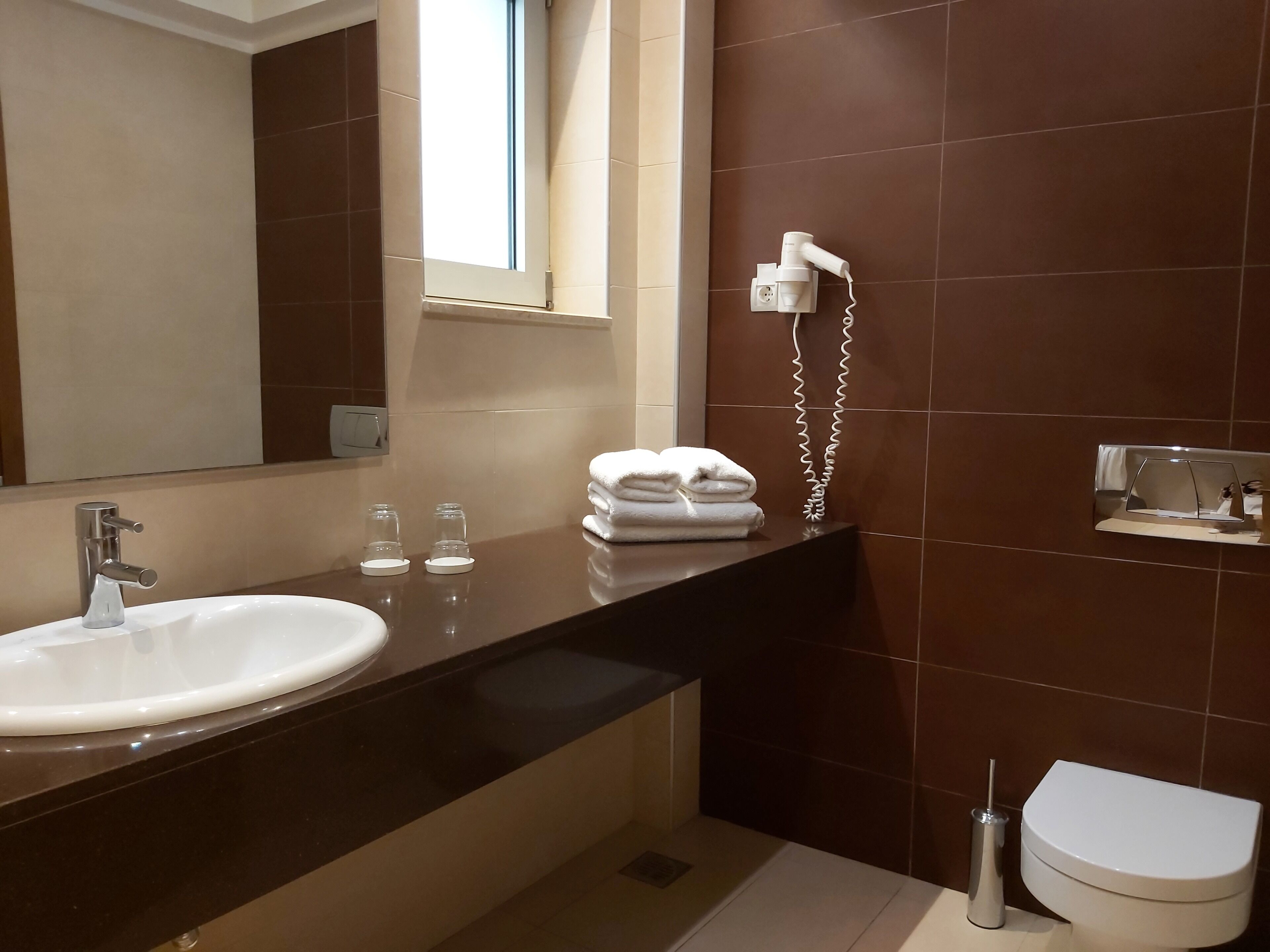 Un baño moderno con un lavamanos grande, un espejo, un perchero para toallas y un inodoro.
