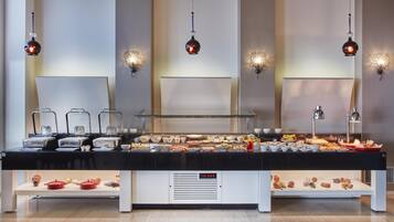 Montaje de bufé con diversas opciones de comida y utensilios de servicio, una barra blanca e iluminación colgante.