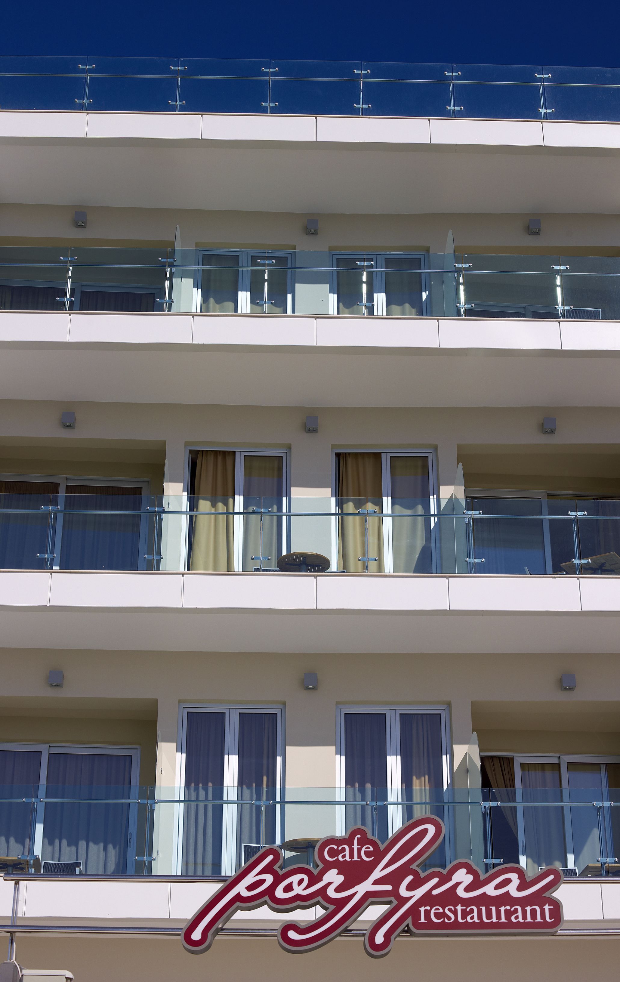 A multi-story building with balconies, a cafe restaurant sign, and windows with curtains.