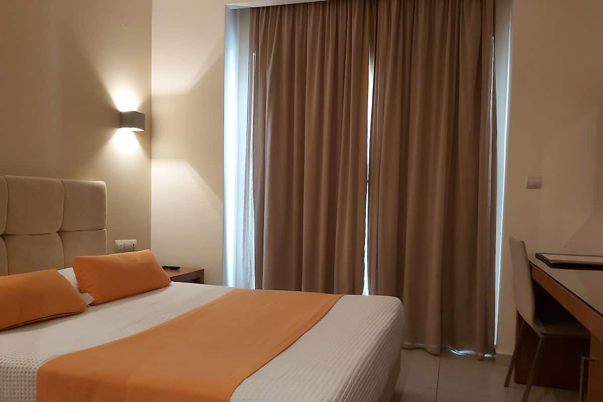 A hotel room with a large bed, an orange bedspread, a desk, and a window with curtains.