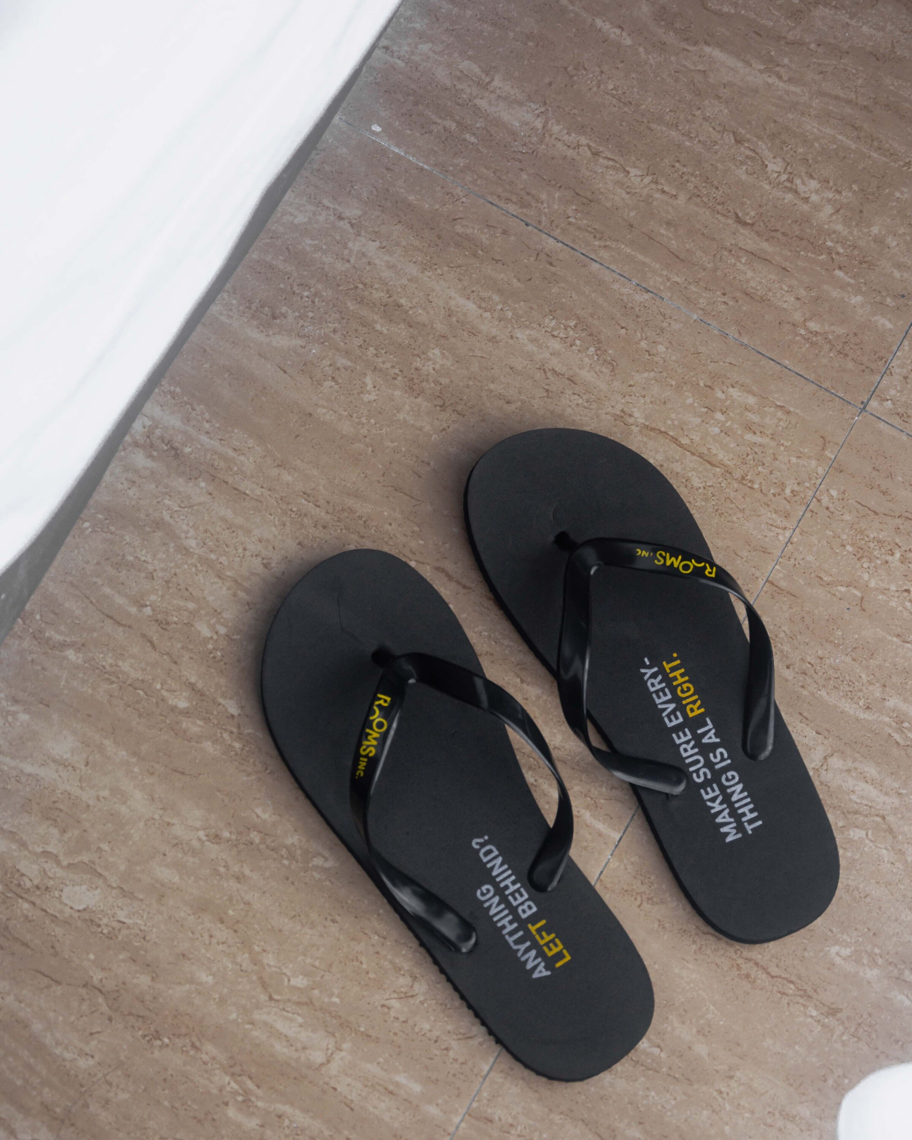 A pair of black flip-flops with text on the sole, placed on a tiled floor.