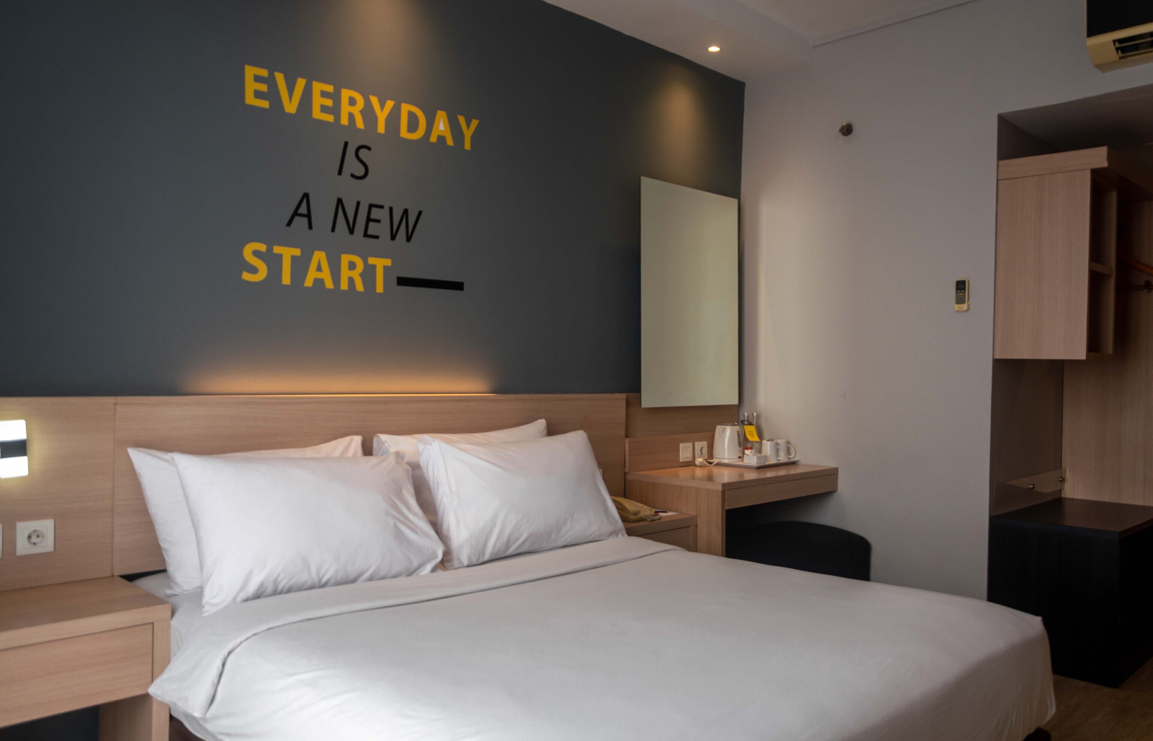 A hotel room with a bed, bedside table, and a motivational quote on the wall.