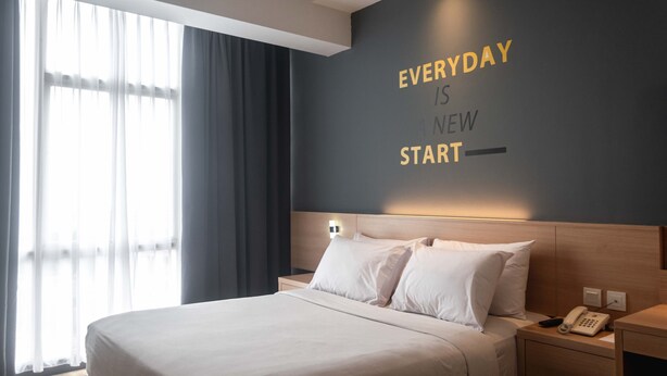 A hotel room with a bed, a bedside table with a phone, and a wall with motivational text. - ROOMS INC d’botanica Bandung (Bandung)