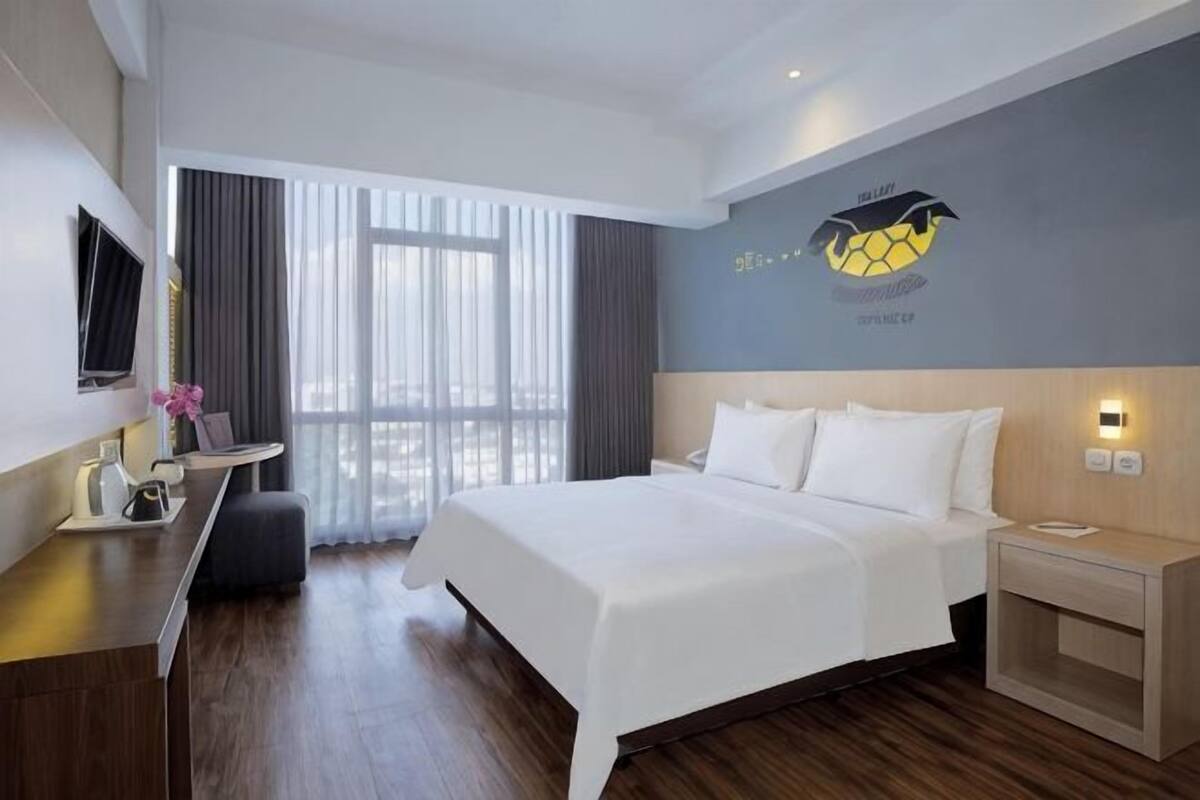 A hotel room with a bed, bedside table, TV, and a window with curtains.