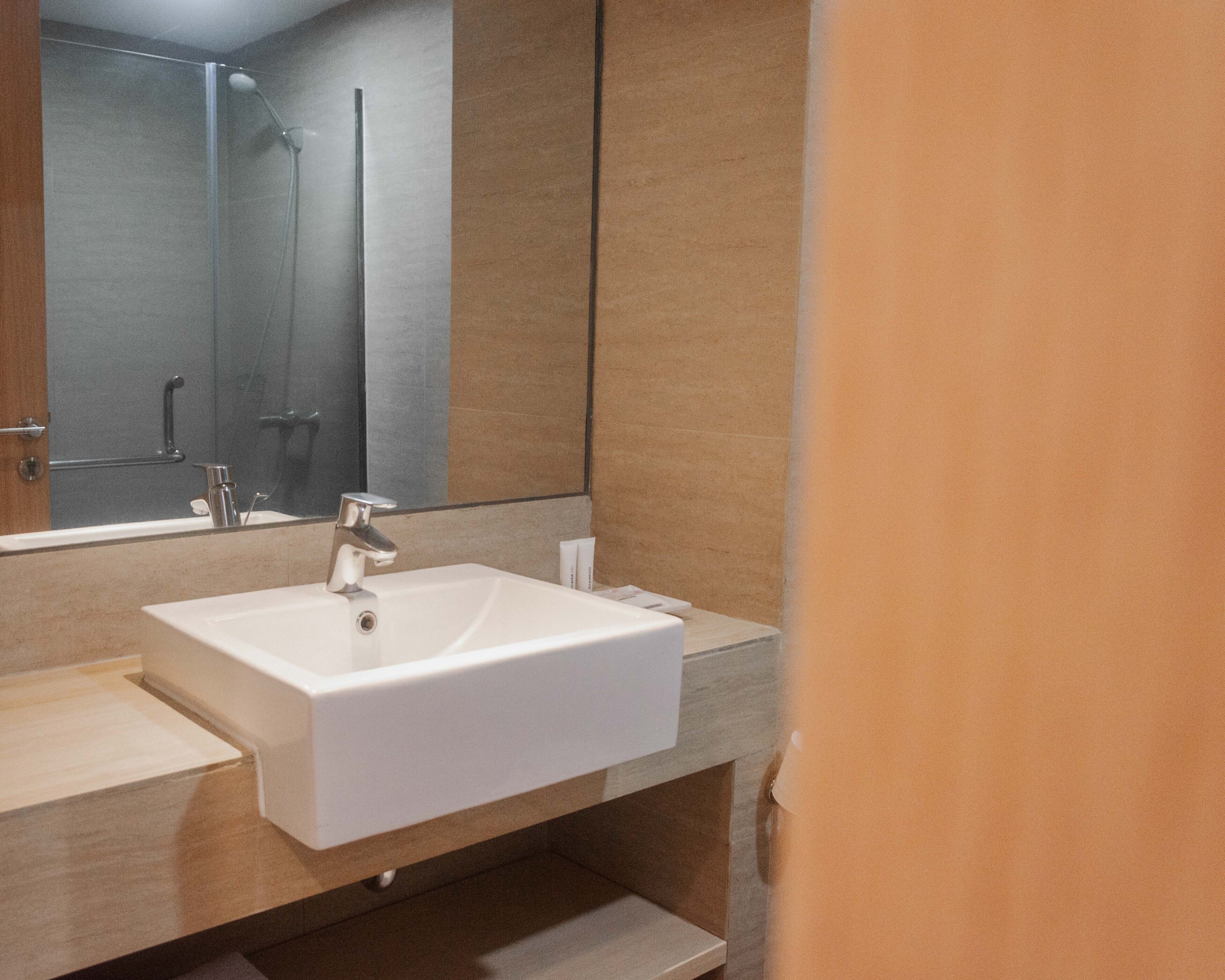 Un bagno moderno con uno specchio grande, un lavandino bianco e una zona doccia.