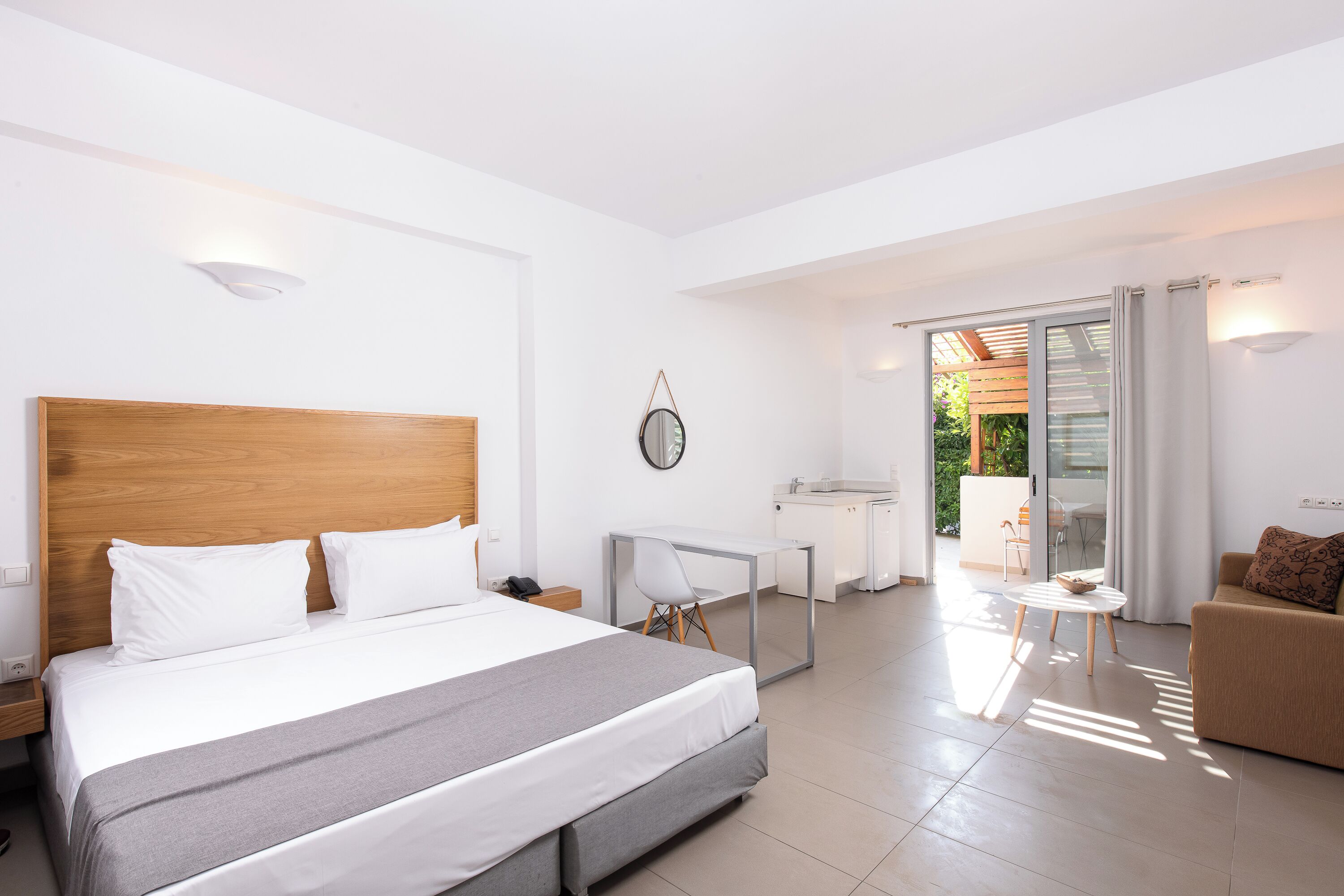 A hotel room with a bed, a desk, a chair, a sofa, and a balcony with a view.