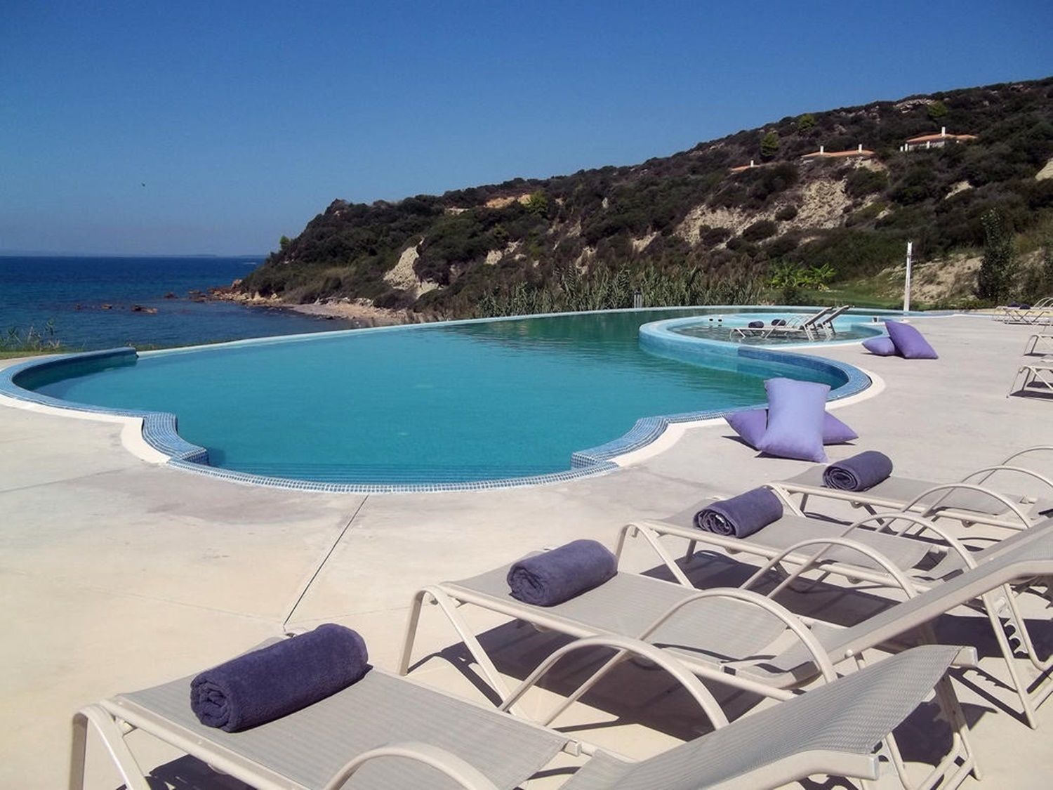 A pool area with lounge chairs and a view of the sea.
