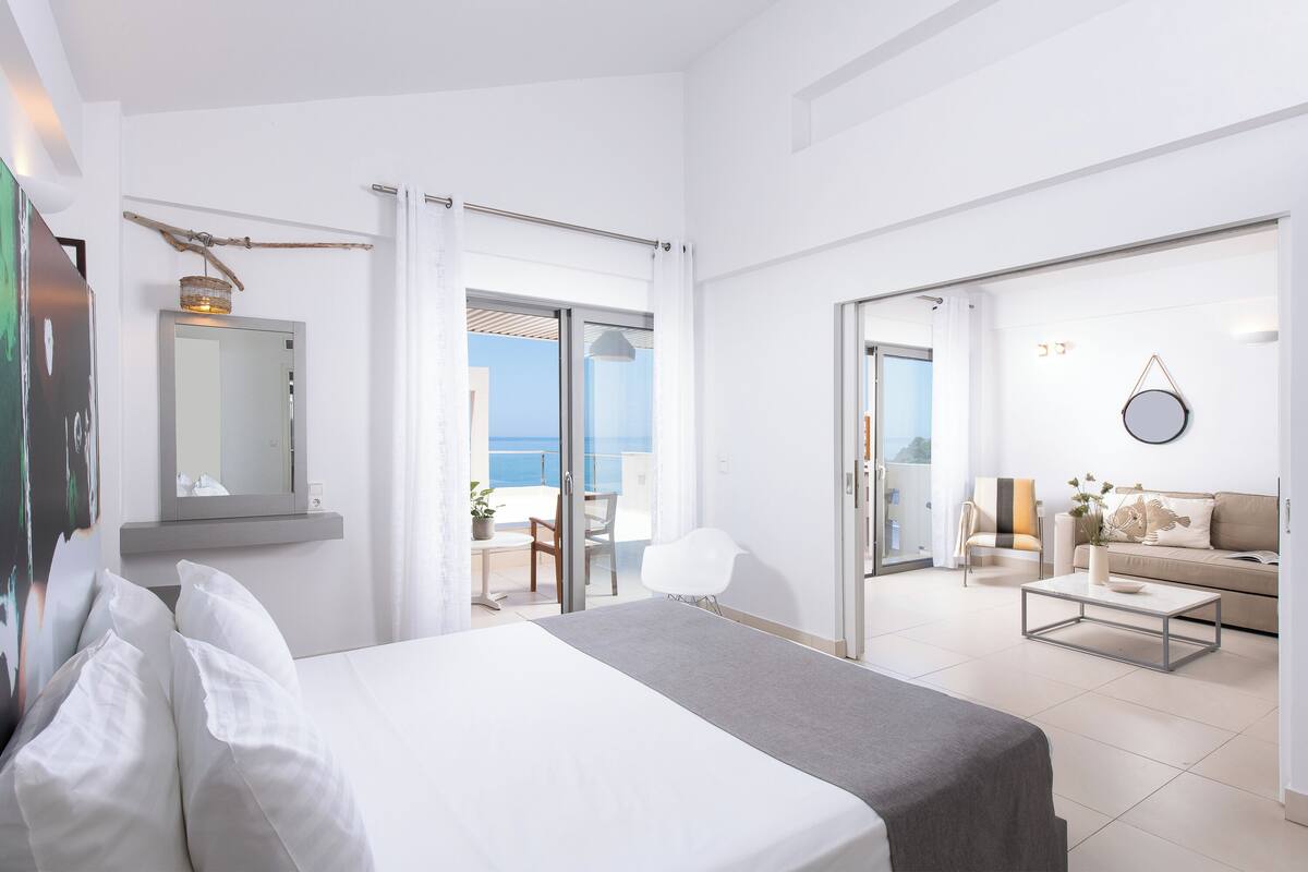 A modern hotel room with a bed, a small table, a sofa, and a balcony with a view.